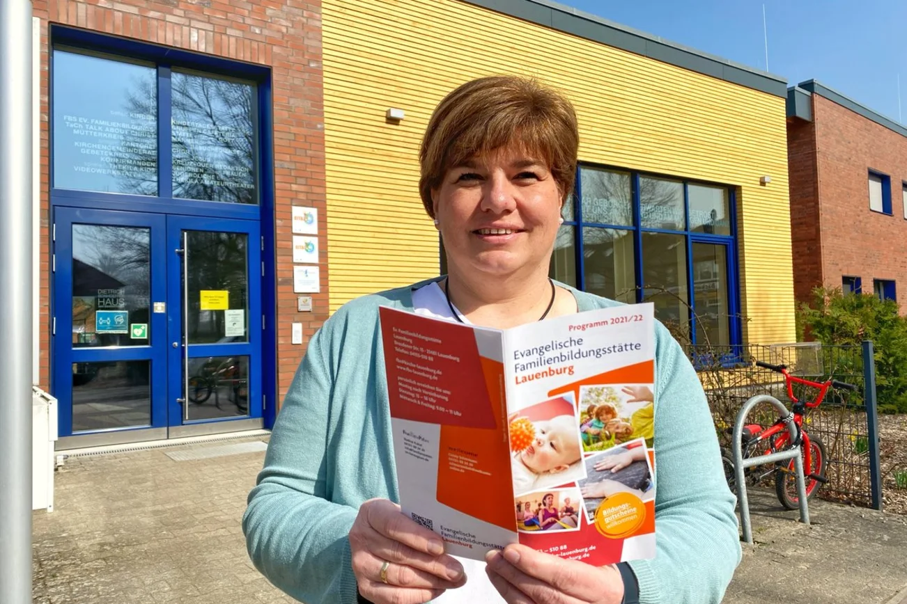 Eine Frau steht mit einem Programmheft vor einem Gebäude. 