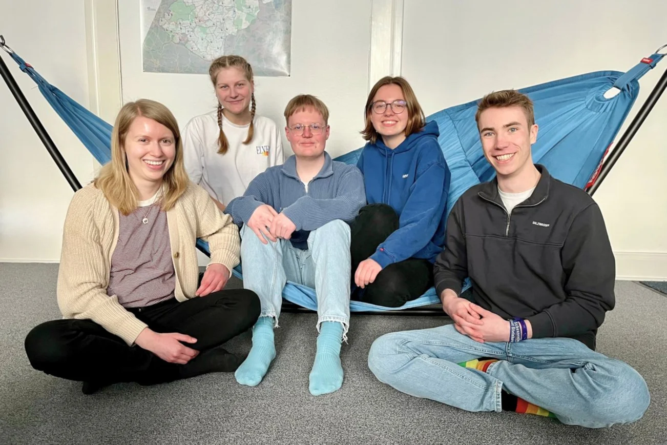 Fünf Jugendliche sitzen in einer Hängematte und auf dem Boden und schauen in die Kamera