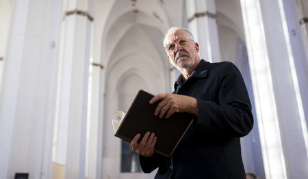 Ein Mann steht in einer Kirche und hält ein Buch in den Händen.