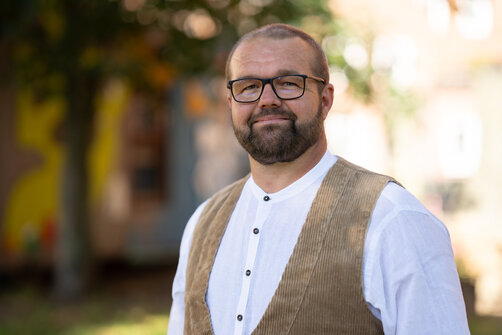Ein Mann mit Handwerkerweste,Brille und Vollbart.