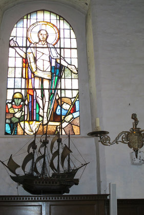 Blick auf ein Kirchenfenster und ein darunter stehendes Segelschiff-Modell