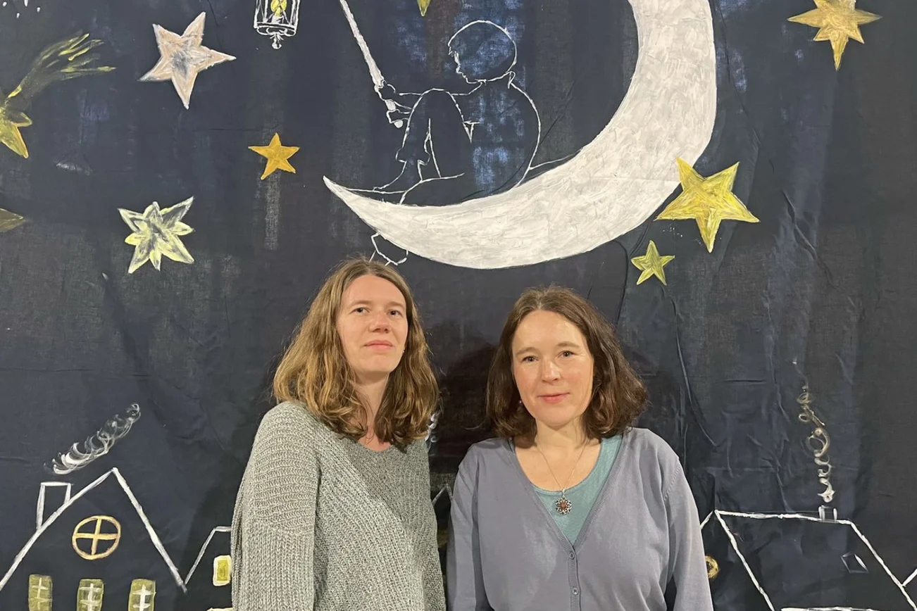 Zwei Frauen stehen vor einem Tuch mit Mond und Sternen.