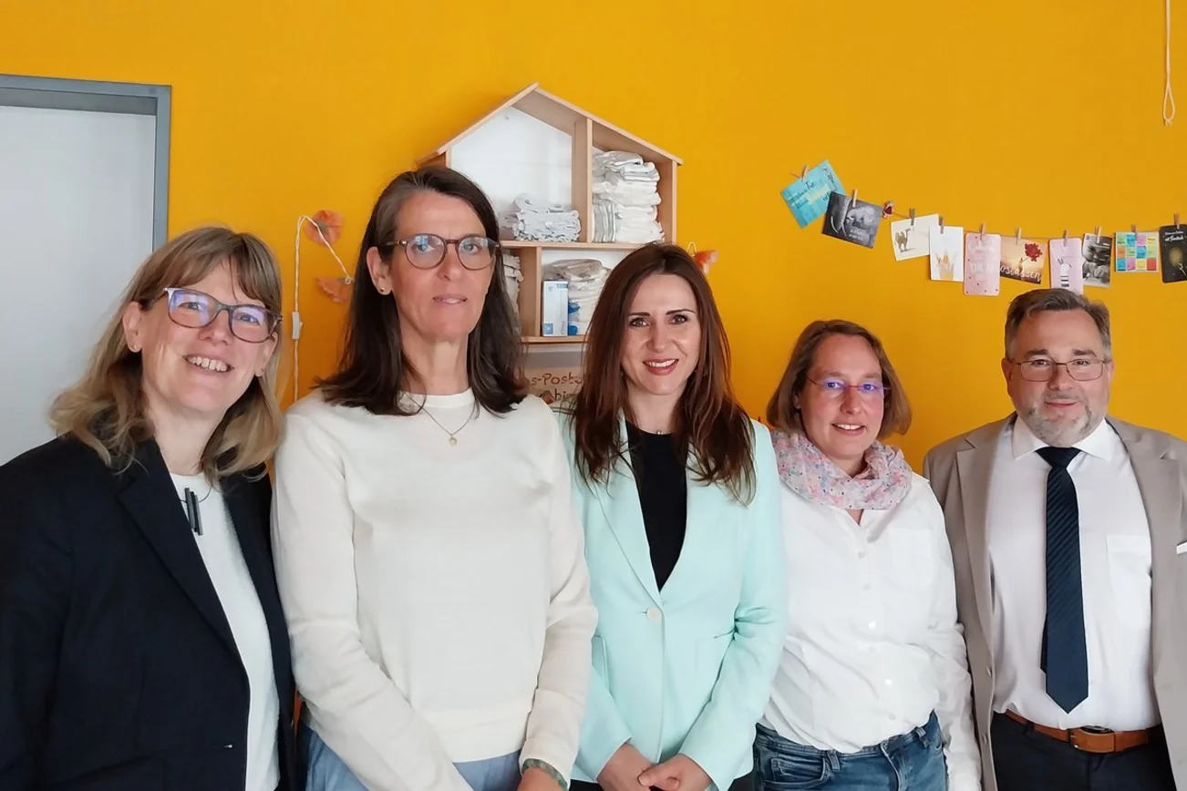 Vier Frauen und ein Mann stehen in einer Reihe vor einer gelben Wand.