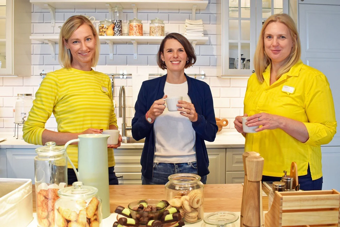 Drei Frauen stehen in einer Küche mit Kaffee und Keksen.