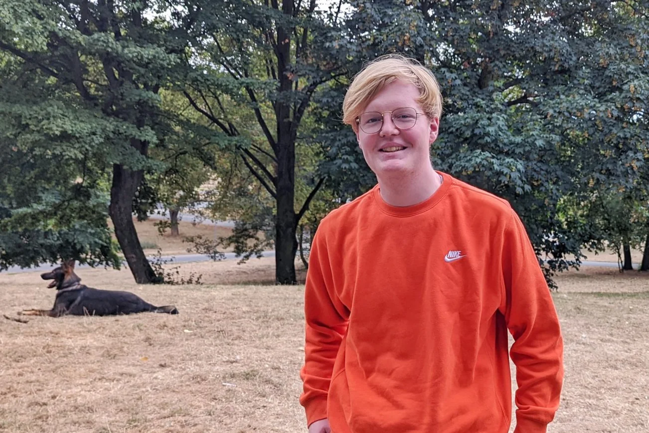 Ein Junger Mann steht vor einem Waldgebiet.