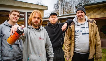 Eine Gruppe junger Männer steht mit Sprayflaschen vor dem alten Gemeindehaus in Wohltorf.