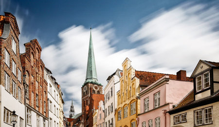 Im Hintergrund ist die St.-Jakobi-Kirche zu sehen. Im Vordergrund die Fassagen links und rechts einer Altstadtstraße Lübecks.