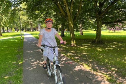 Pröpstin Kallies sitzt mit einem Fahrradhelm auf dem Kopf in einem begrünten Park auf dem Fahrrad. - Copyright: Katharina Micheel