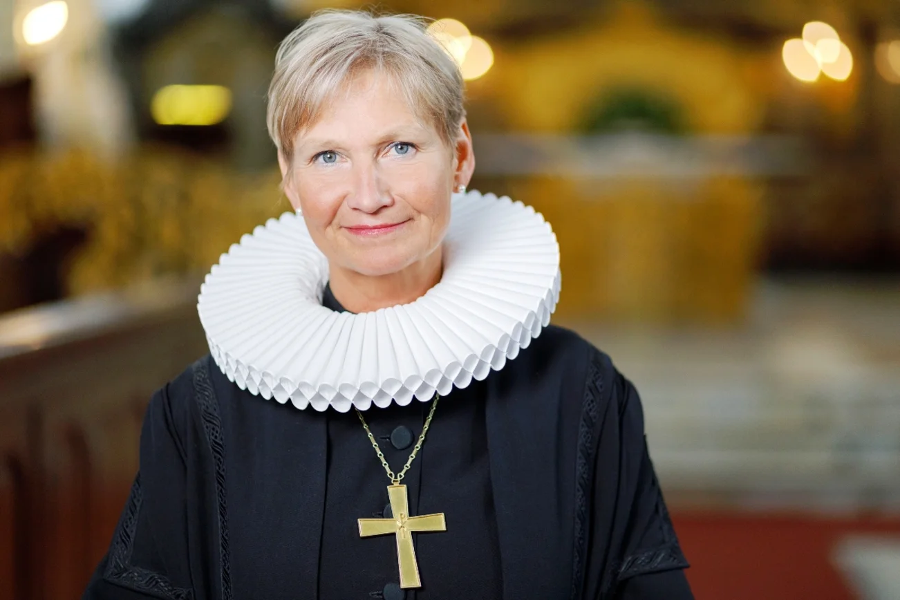Eine Frau mit Talar, weißem Rundkragen und goldenem Bischofskreuz blickt freundlich in die Kamera.
