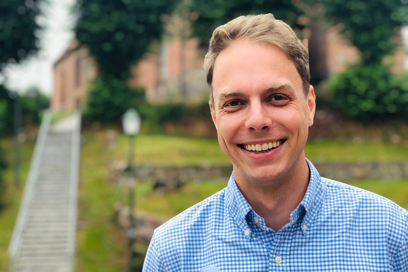 Mann steht vor einer Kirche und lächelt. 