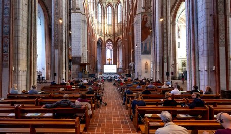 Der Innenraum einer großen Kirche. Menschen sitzen auf Abstand in den Bänken.