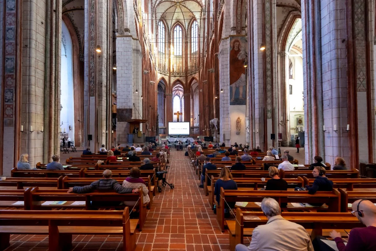 Der Innenraum einer großen Kirche. Menschen sitzen auf Abstand in den Bänken.