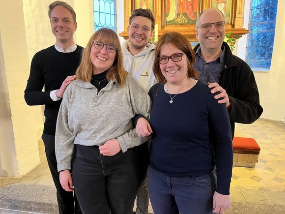 Fünf Personen stehen lächelnd in einer Kirche.