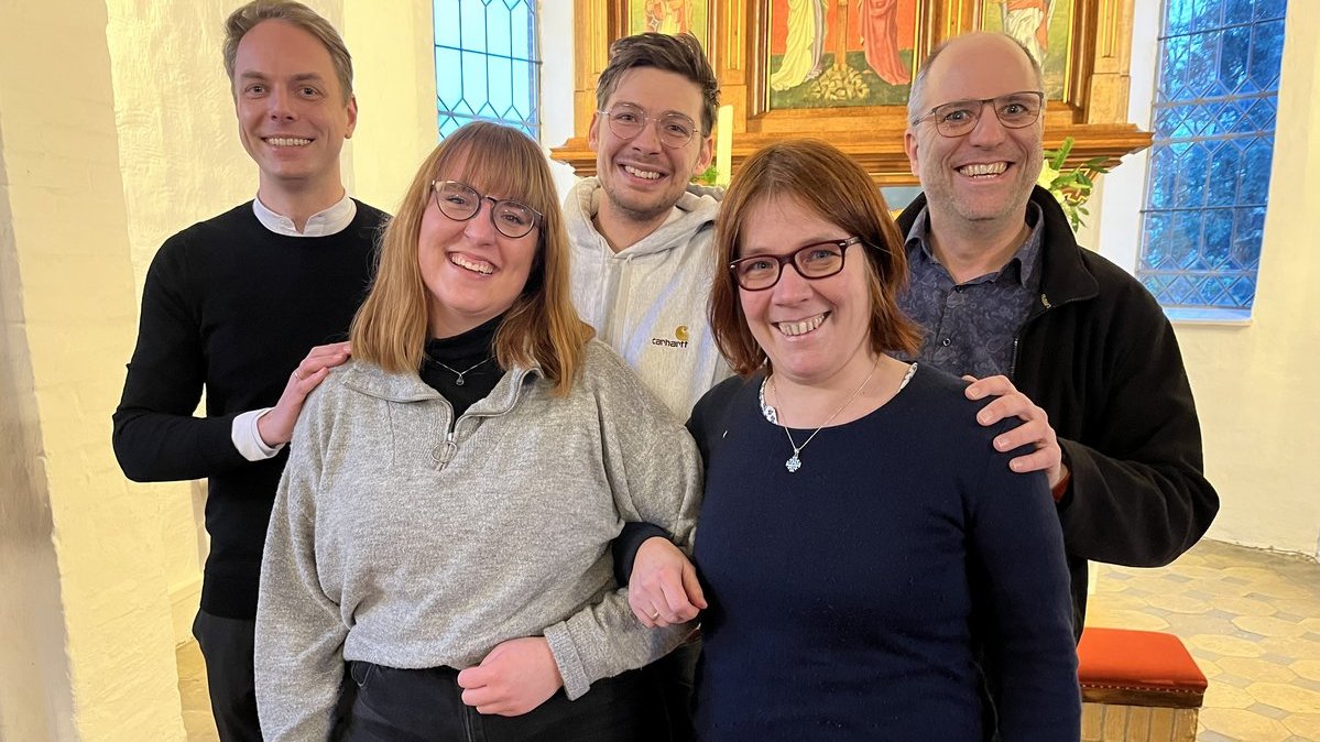 Fünf Personen stehen lächelnd in einer Kirche.