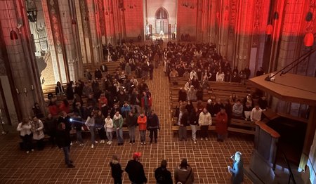 Ein rot erleuchtetes Kirchenschiff mit vielen jungen Leuten.