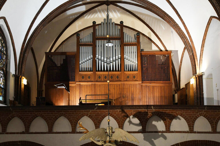 Eine Orgel auf einer Empore mit braunem Holz. Die Pfeifen ragen in der Mitte in die Höhe