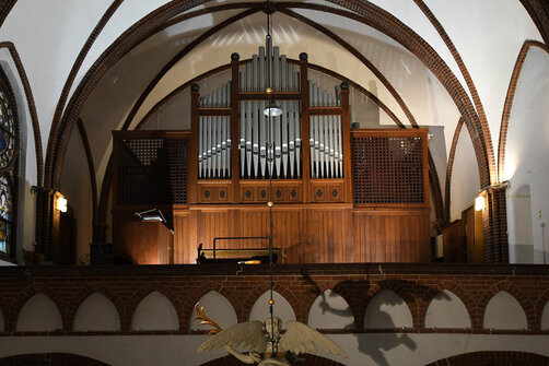 Eine Orgel auf einer Empore mit braunem Holz. Die Pfeifen ragen in der Mitte in die Höhe
