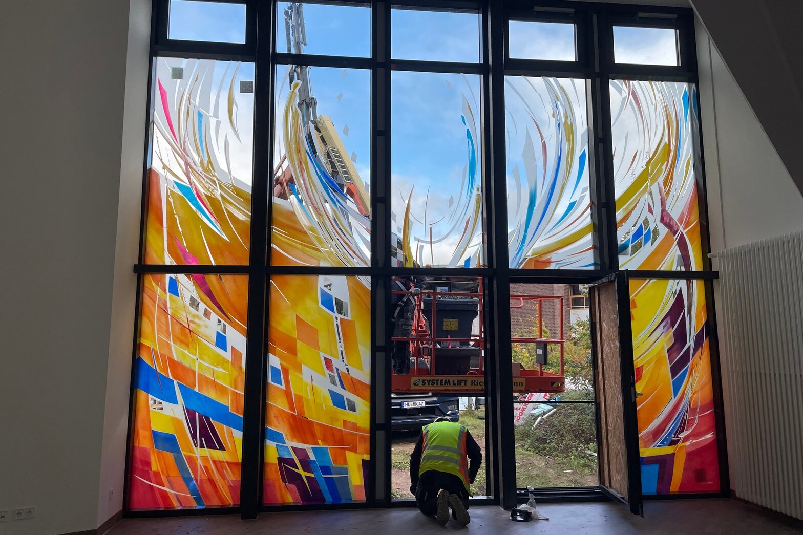 Blick aus den dem raum auf die Fenster. Im unteren Bereich sitzt ein Monteur und bereitet die Montage des letzten Fensters vor.
