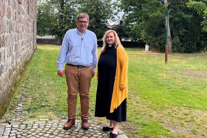 Pastorin Poepping und Pastor Gienke stehen vor einer Mauer und lächeln in die Kamera. - Copyright: Katja von Kiedrowski