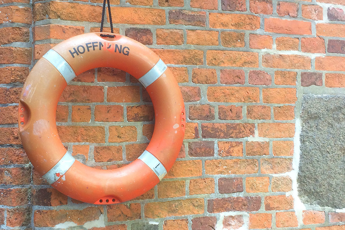 Ein älterer oranger Rettungsring mit Nutzungsspuren hängt an einer Backsteinwand.