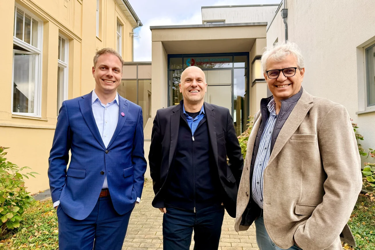 Drei Männer lächeln vor einem Gebäude