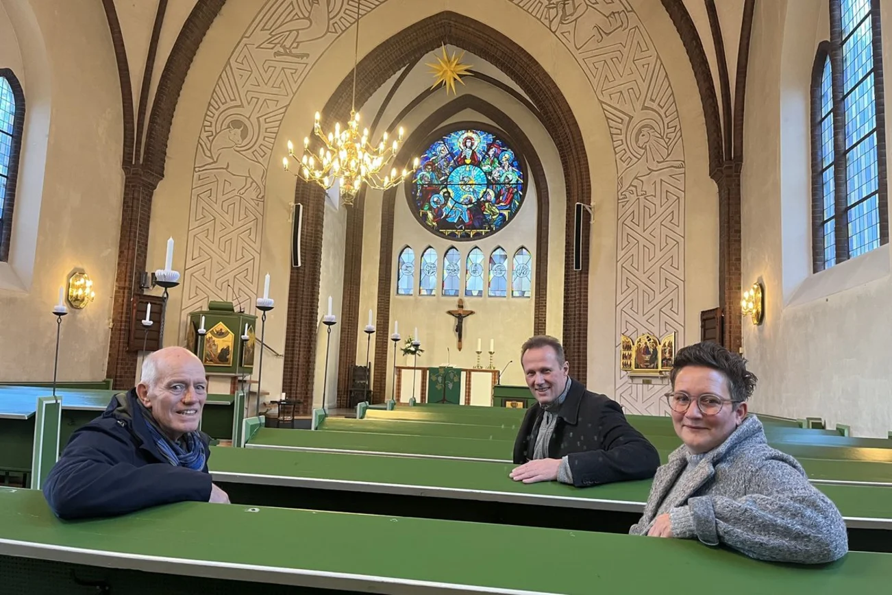 Zwei Männer und eine Frau sitzen in einer Kirchenbank.