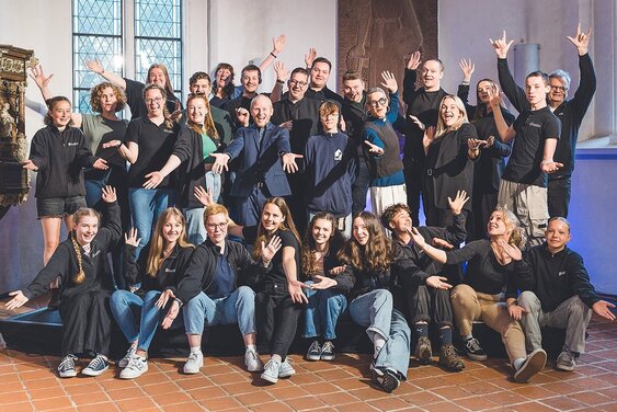 Eine Gruppe von Menschen stehen und sitzen hintereinander, einige haben die Arme hochgestreckt - Copyright: Guido Kollmeier