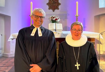 Zwei Menschen in Talaren. Im Hintergrund der Altar einer Kirche. - Copyright: Kirchenkreis Lübeck-Lauenburg