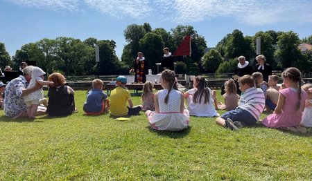 Das Tauffest 2023 im Altstadtbad Krähenteich. Vorne sind Kinder mit ihren Familien sitzend, im Hintergrund Pastorinnen und Pastoren zu sehen. 