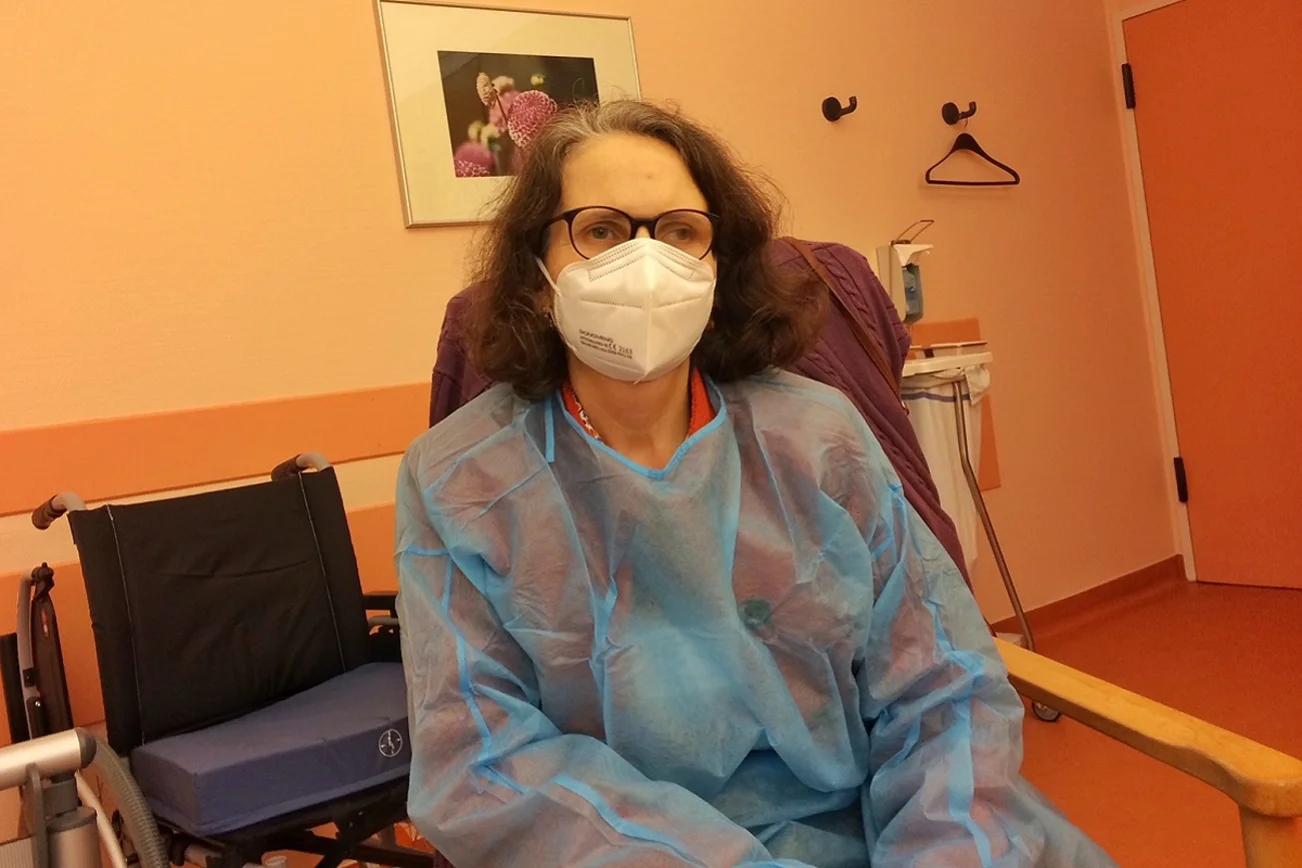 Eine Pastorin sitzt in Klinikkleidung in einem Krankenhaus. 