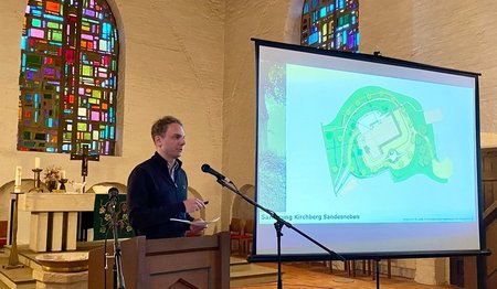 Mann am Mikrofon neben Beamer-Leinwand