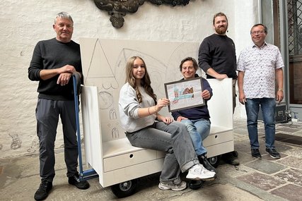 Fünf menschen sitzen auf und stehen um die noch unbemalte Kirchenbank herum und lächeln in die Kamera - Copyright: Katharina Micheel