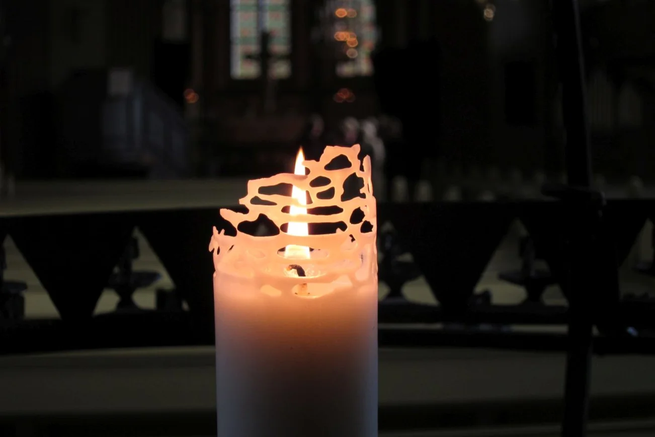 Eine brennende weiße Kerze in einer dunklen Kirche. 