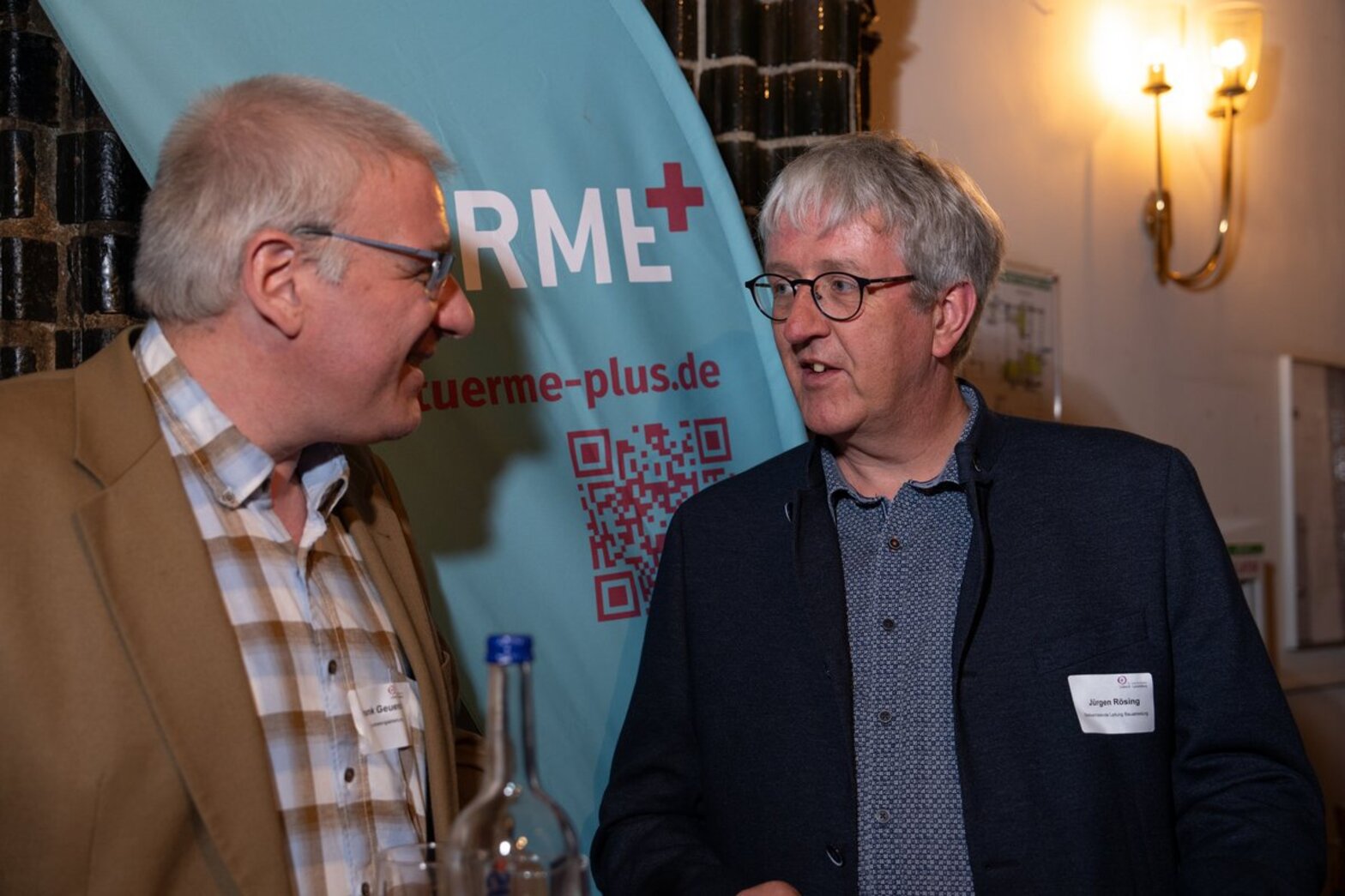 Zwei Männer stehen vor einem Banner und unterhalten sich. 