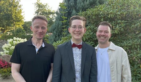 Drei Männer stehen draußen und lächeln für die Kamera.