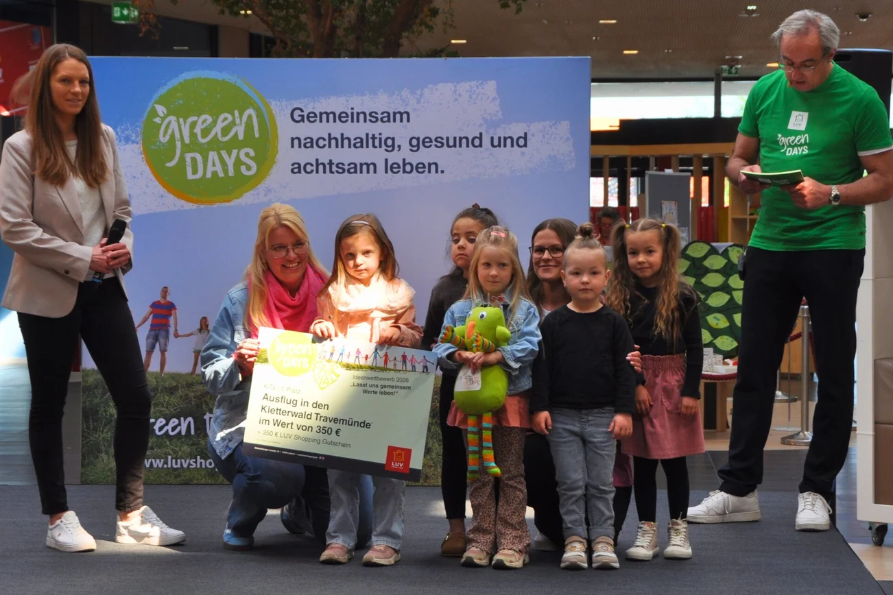 Eine Gruppe von Kleinkindern steht zusammen mit Erzieherinnen auf einer Bühne und hält einen großen Pappcheck.