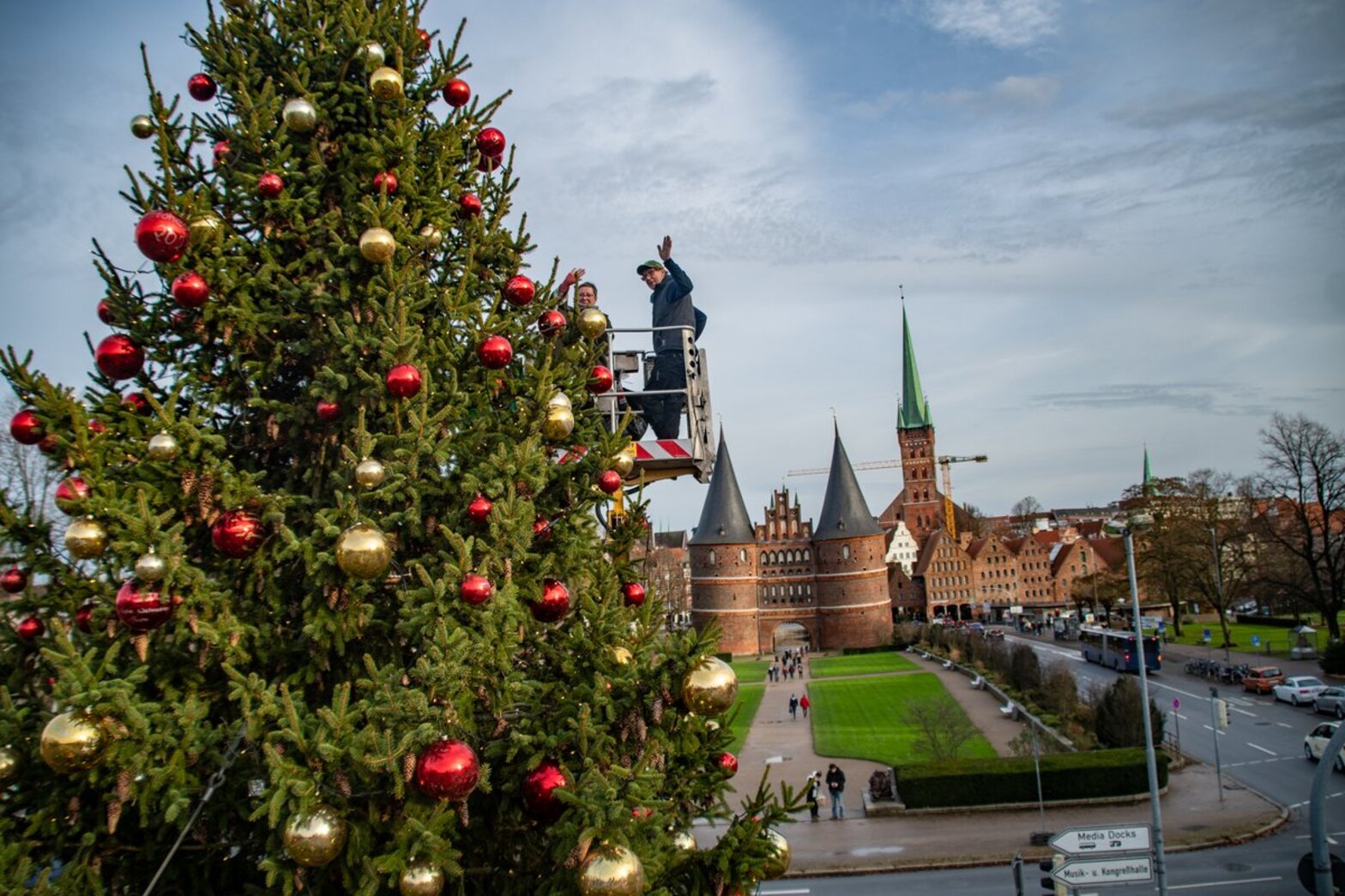 Ein großer Weihnachtsbaum mit roten und goldenen Kugeln, im Hintergrund das Holstentor und St. Petri von Lübeck