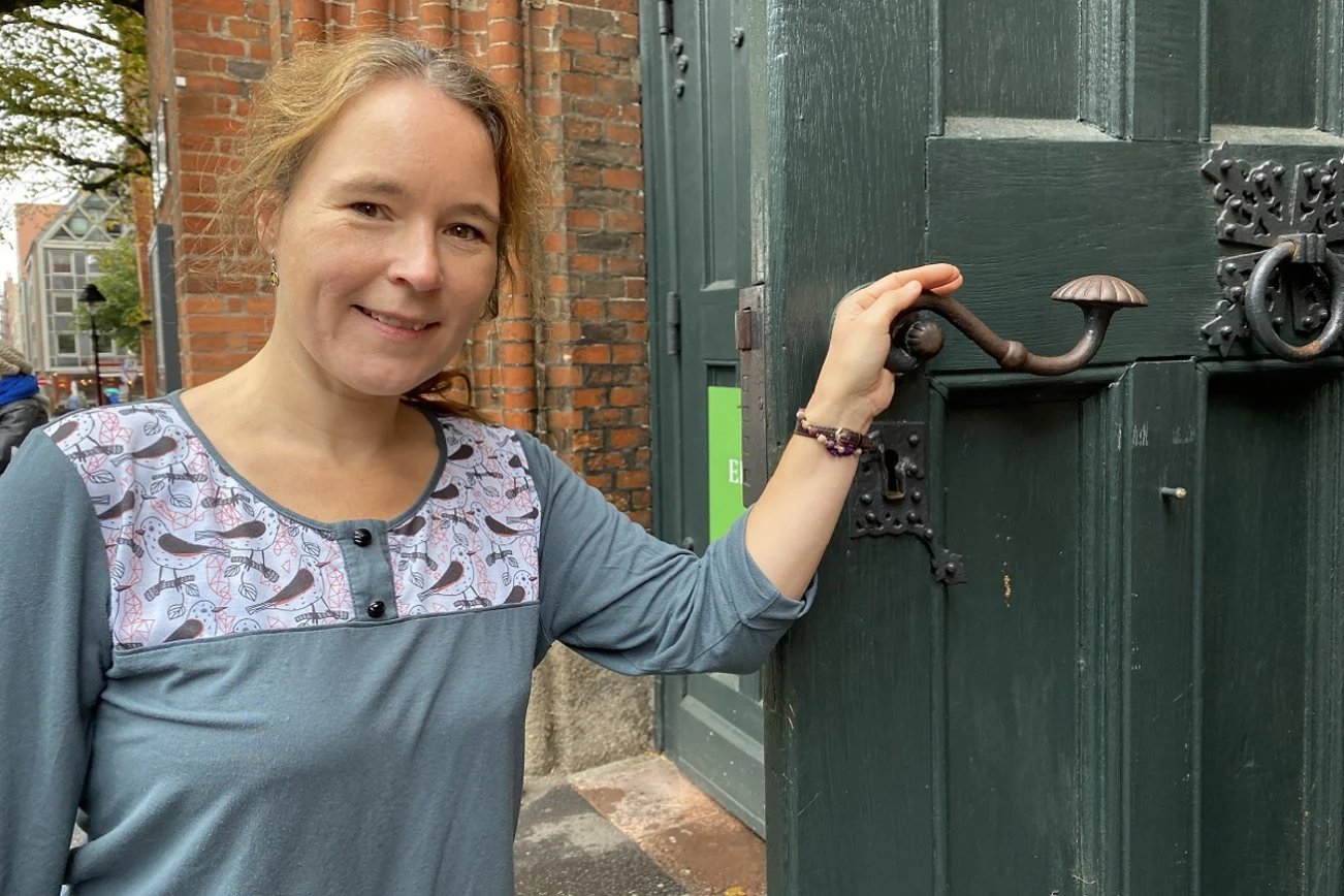 Frau steht an einer Kirchentür und öffnet diese