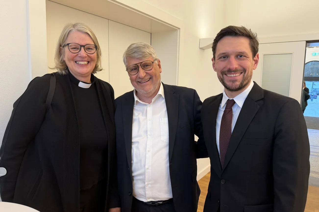 Eine Frau und zwei Männer lächeln in die Kamera.