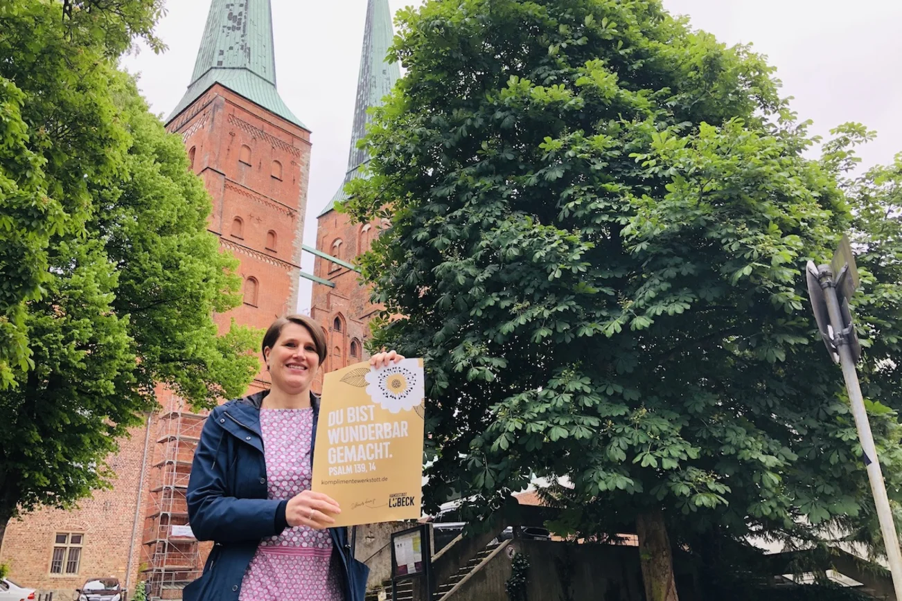 Pastorin Margrit Wegner mit dem Komplimente-Plakat vor dem Dom zu Lübeck.