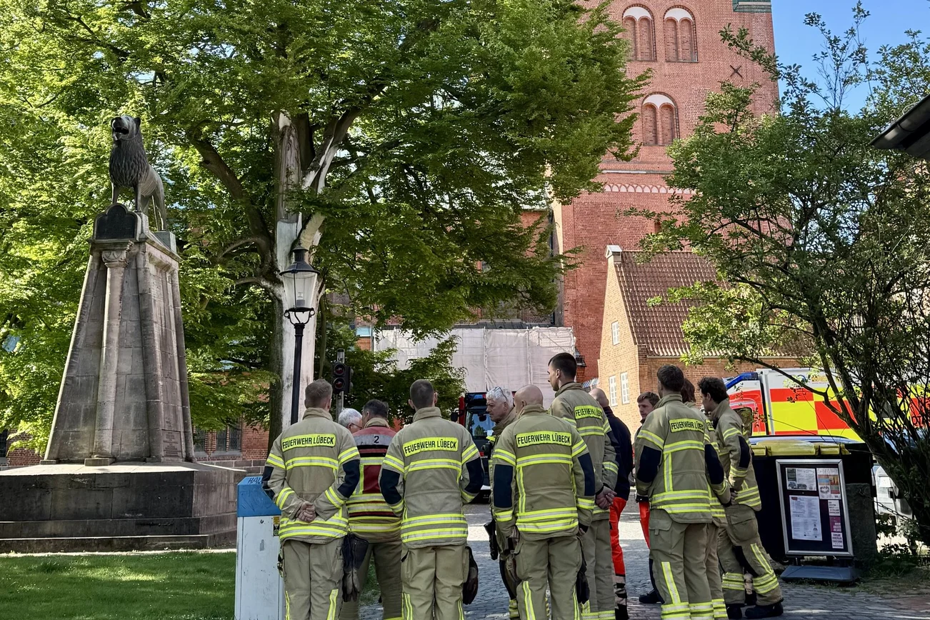 Mehrere Feuerwehrleute stehen draußen vorm Lübecker Dom.