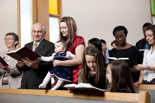 Mehrere Personen unterschiedlichen Alters sind in einem Gottesdienst und halten ein Liederbuch vor sich aufgeschlagen. 