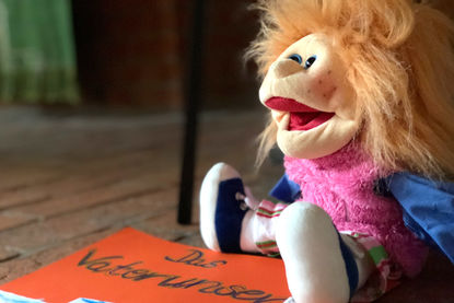 Larissa Funk - Copyright: Ev.-Luth. Kirchenkreis Lübeck-Lauenburg Eine Handpuppe mit langen Haaren, sitzt recht in der Ecke auf einem roten Pappschild, auf welchem 'Das Vaterunser' steht - Copyright: Ev.-Luth. Kirchenkreis Lübeck-Lauenburg