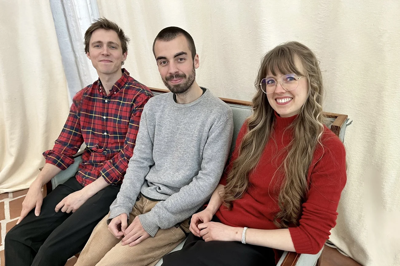 Drei Menschen sitzen auf einer Couch.