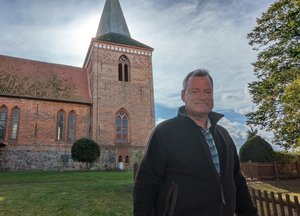 Ein Mann steht vor einer Kirche und schaut in die Kamera.