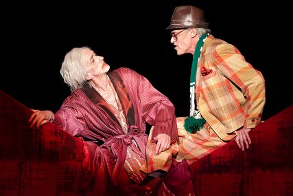 Zwei Männer in schrillen Kostümen sitzen sich gegenüber. - Copyright: Theater Lübeck