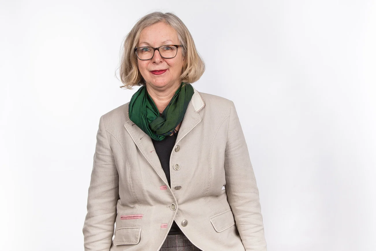 Eine Frau steht vor einer weißen Leinwand und blickt in die Kamera. 