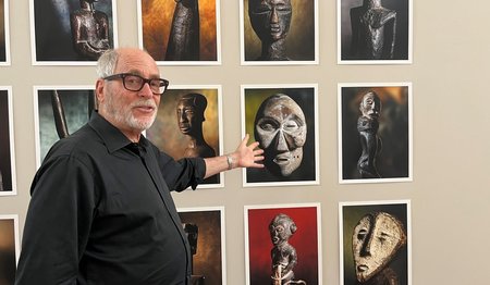 Ein älterer Mann mit schwarzer Brille steht vor einer Wand mit Fotografien