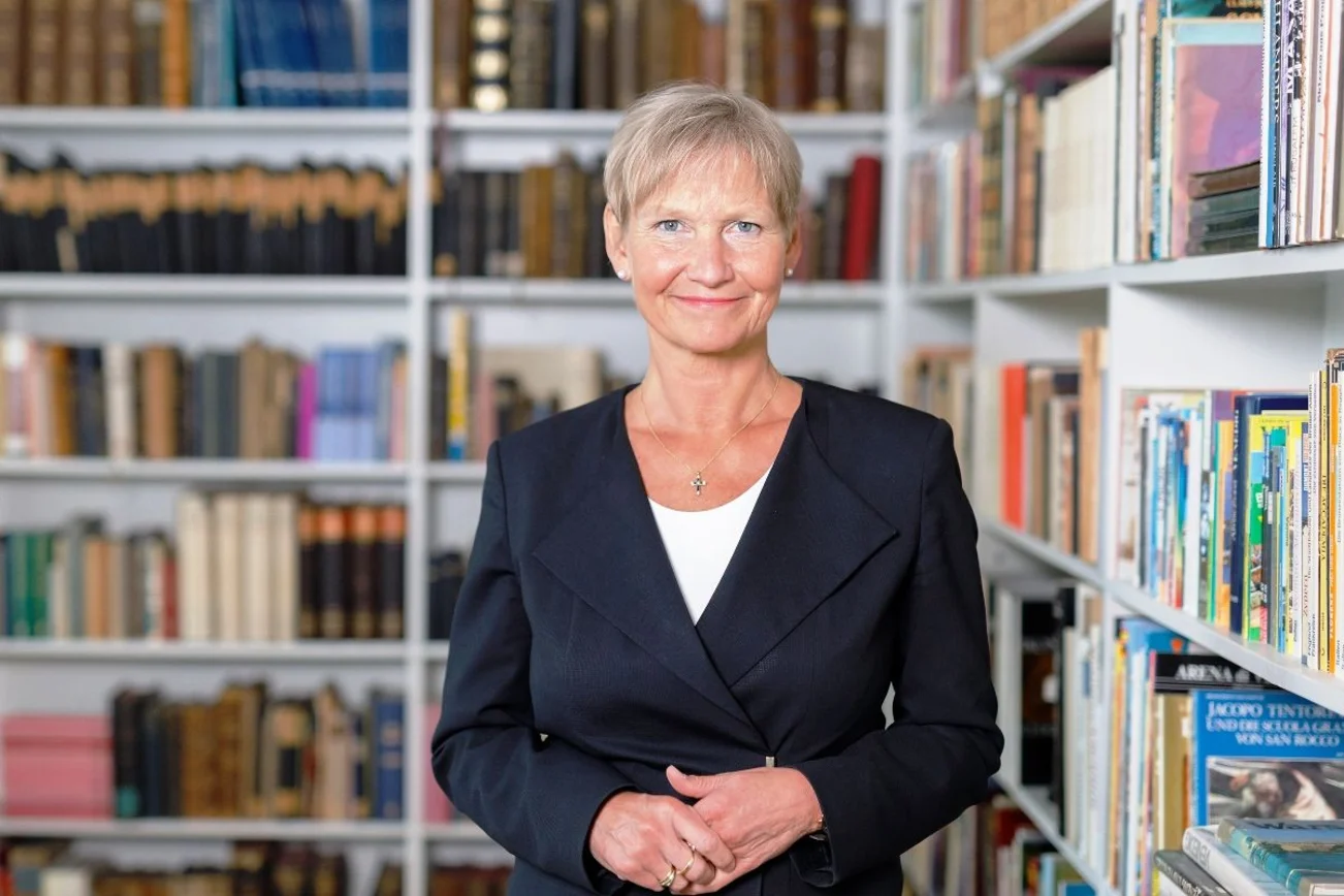 Bischöfin Kirsten Fehrs schaut in die Kamera. Im Hintergund Regale mit Büchern.