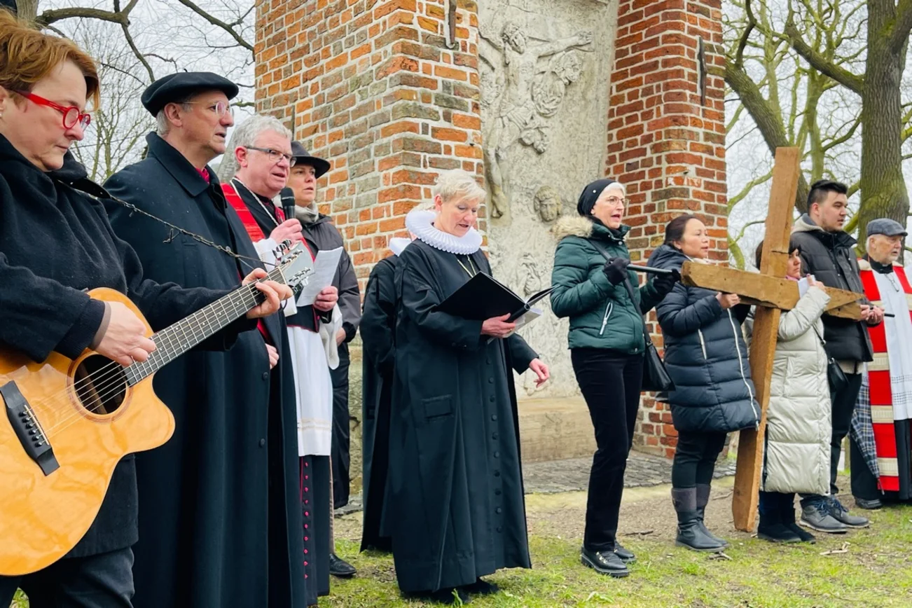 Mehrere Menschen stehen vor einem auf vor Darstellung der Kreuzigung Jesu und singen.